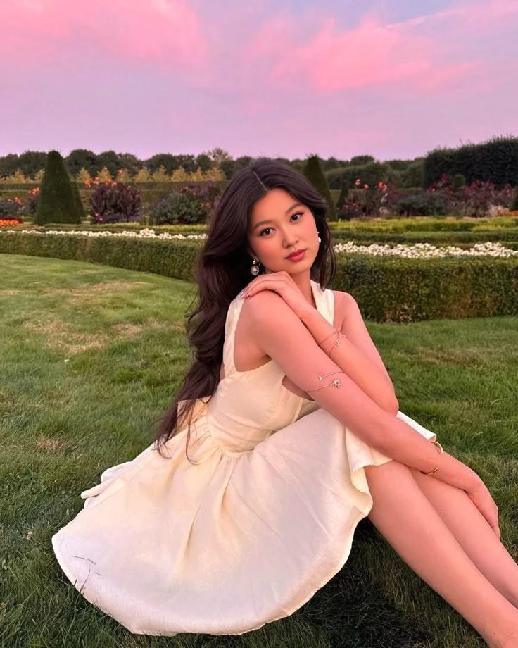 Kim Ji-hye sentada en un campo verde contemplando una puesta de sol.